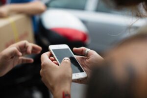 Close-up of hands holding a white smartphone as a group gathers around in the background, out of focus.