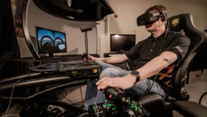 Person in a flight-simulator cockpit wearing a VR headset, gripping control levers and surrounded by screens and panels